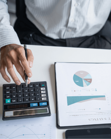 Pessoa usando calculadora sobre mesa com relatório financeiro contendo gráfico de pizza e gráfico de barras, representando a análise e comparação de investimentos de renda fixa